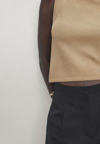 Beige ribbaus sleeveless toppi, jossa on pyöreä pääntie, yhdistetty tummiin räätälöityihin housuihin. Suuri tekstuuri ja minimalistiset design-yksityiskohdat.