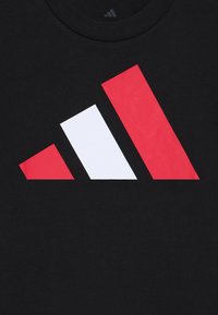 Μαύρο βαμβακερό t-shirt με μεγάλη γραφική παράσταση από κόκκινες και λευκές γεωμετρικές σχήματα, συμπεριλαμβανομένων δύο κεκλιμένων ορθογωνίων και ενός τριγώνου.