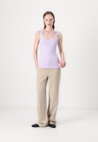 Lila tanktop met brede banden, gecombineerd met beige wijde broekspijpen. De outfit wordt aangevuld met zwarte platte schoenen. Over het geheel een gladde stoftextuur.
