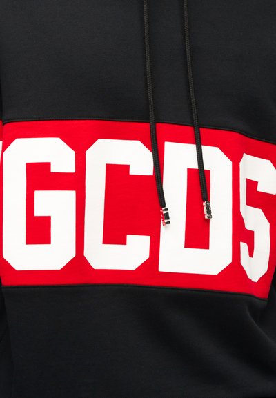Felpa con cappuccio nera con una larga striscia rossa sul petto che mostra grandi lettere bianche in grassetto "GCDS" e cordoncini neri con punte metalliche.
