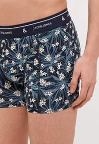 Námořnické boxerské šortky s květinovým vzorem obsahujícím žluté a bílé květy, vyrobené z elastického materiálu, s elastickým pasem s logem.