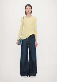 Yellow long-sleeve henley top paired with wide-leg dark denim jeans, complemented by a small blue handbag and white shoes.
