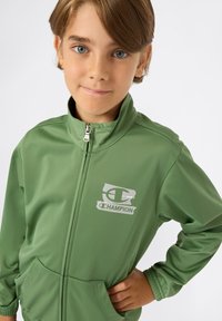 Groene sportjack met volledige ritssluiting, voorzien van een hoge kraag en twee voorzakken. "Champion" logo in het wit op de linkerborst.