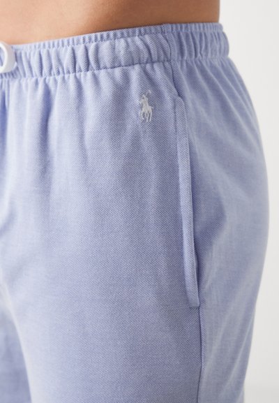 Light blue cotton sweatpants with an elastic waistband, featuring side pockets and a small, white embroidered logo on the left thigh.