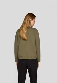 Olive green quilted jacket with a round neckline, long sleeves, and a textured surface, paired with black trousers.