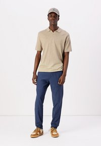 Camisa polo beige, pantalones navy y zapatillas color tostado. La gorra coincide con el color de la camisa. Diseño simple con mangas cortas y corte relajado.