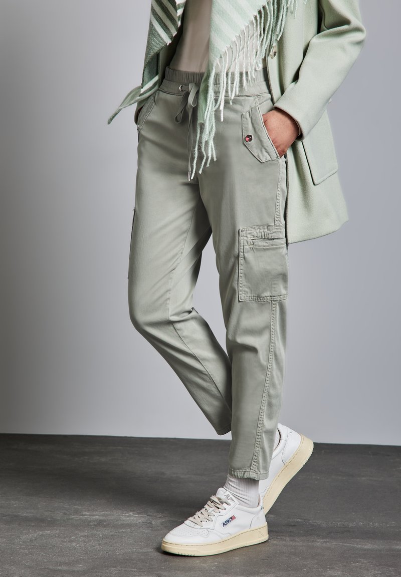 Lässige hellgrüne Cargo-Hosen mit elastischem Bund und mehreren Taschen, kombiniert mit weißen Sneakers. Weiches Material und praktisches Design.