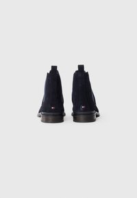 Ein Paar marineblaue Wildleder- Chelsea-Boots mit Zuglaschen und kleinem Logo an der Ferse, von hinten auf einem weißen Hintergrund gezeigt.