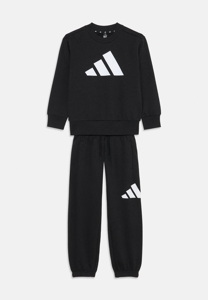 Čierna mikina a súprava teplákov vyrobená z bavlny. Mikina má veľké biele logo Adidas; tepláky majú menšie logo na nohavici.
