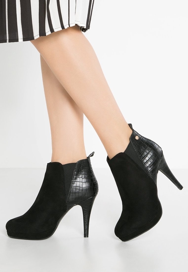 Botines negros con parte trasera de cuero brillante y estampado, parte superior de ante y un tacón de aguja de 10 cm. Presentan paneles laterales elásticos para facilitar su uso.