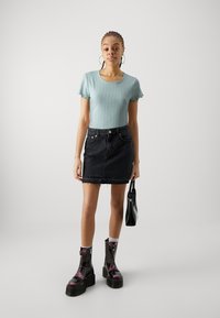 Haut bleu clair à manches courtes côtelé, mini jupe en denim noir avec ourlet effiloché, bottes chunky zippées noires et violettes, sac à main noir.