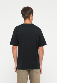 Sorte kortærmede t-shirt lavet af bomuld, med en klassisk rund hals og almindelig pasform, vist fra bagsiden.