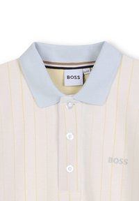 Polo à manches courtes en crème avec un col bleu clair et de subtils rayures jaunes. Comprend trois boutons blancs et un logo "BOSS" brodé.