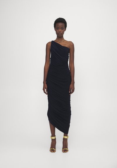 Vestido azul marino de un solo hombro con tejido fruncido, ajuste ceñido, longitud a mitad de pantorrilla, combinado con tacones dorados de tira en el tobillo y un collar simple.