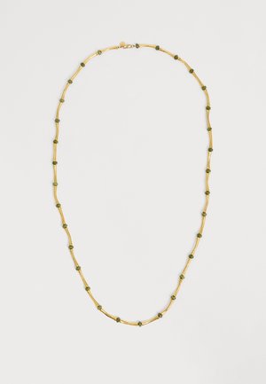 Goldene Halskette mit gleichmäßig verteilten kleinen grünen Steinperlen auf hellem neutralem Hintergrund.
