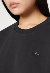 Black cotton sweatshirt with a round neck and short sleeves. Features a subtle dark embroidered logo on the chest. Smooth texture.