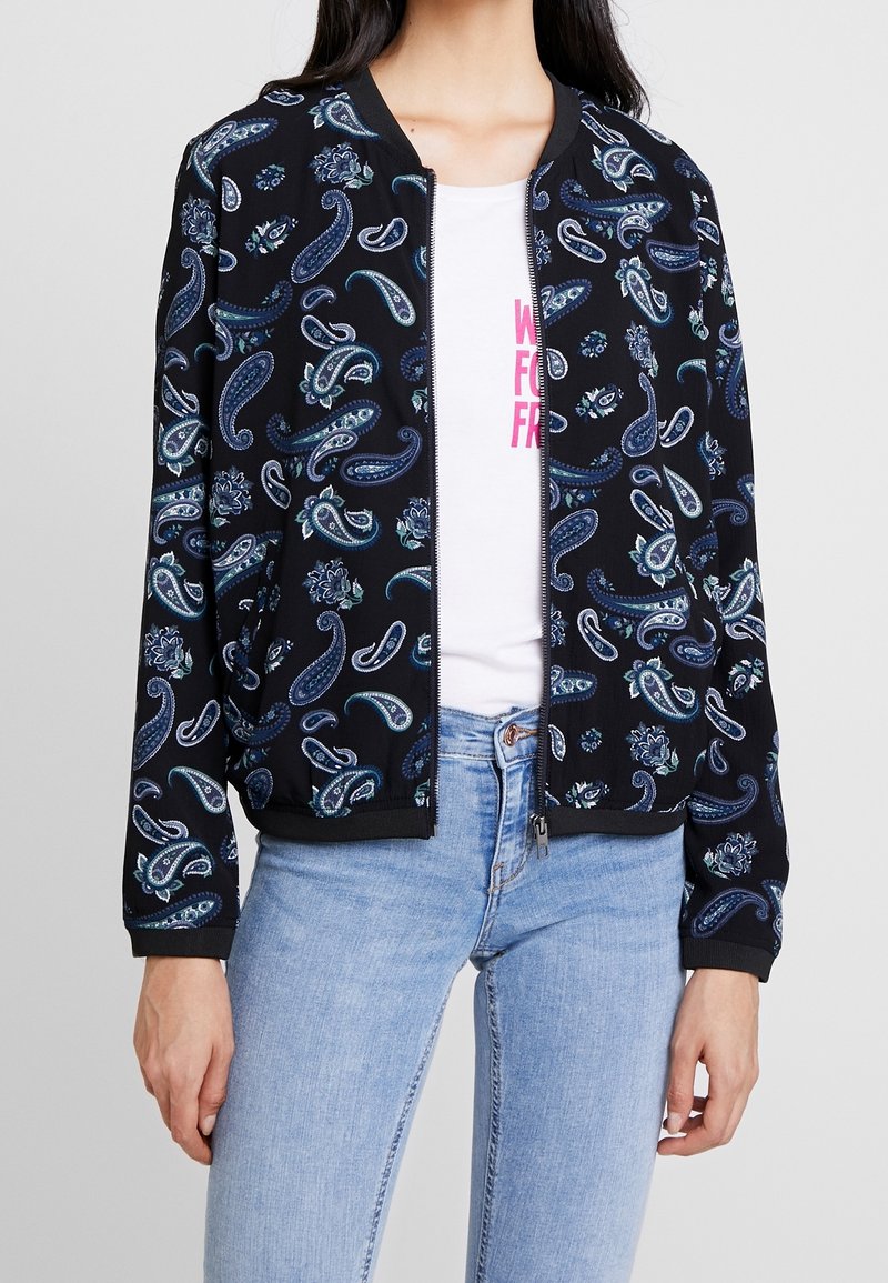 Svart bombarjacka med ett paisleymönster i blå och gröna nyanser. Ribbat manschetter och nederkant, dragkedjestängning, bärs över en vit T-shirt.