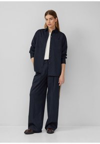 Ensemble chemise et pantalon à rayures navy en tissu tissé. Coupe ample. La chemise possède des boutons et deux poches avant, le pantalon a des jambes larges.
