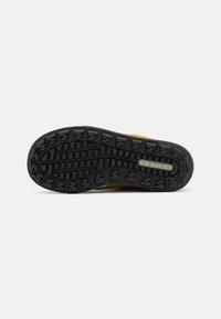Semelle extérieure en caoutchouc noir avec des creux profonds, arborant le logo "MERRELL" ; semelle intermédiaire jaune uni avec des accents texturés.