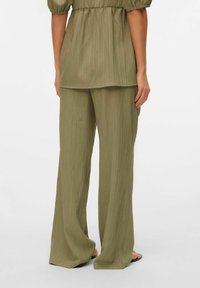 Pantalons larges texturés en vert olive associés à un haut ample assorti, avec des manches bouffantes et une taille froncée.