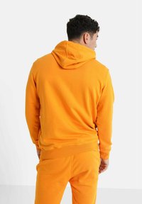 Sudadera con capucha naranja hecha de tela suave, con un bolsillo tipo canguro y puños acanalados. Textura lisa con un ajuste relajado.
