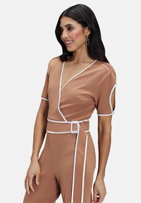 Brown wrap jumpsuit with short sleeves, white trim, and belt detail. Features a deep V-neckline and side cutouts for added design.