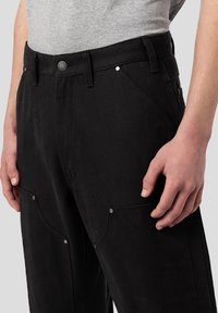 Svarta bomullsbyxor med en texturerad yta, har en midja med en metallknapp och sidofickor, detaljerade med silverfärgad accenter.