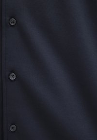 Navy Button-Up-Hemd mit glatter Textur, versehen mit schwarzen Knöpfen und einem klassischen Design. Nahaufnahme, die die Stoff- und Knopfdetails hervorhebt.