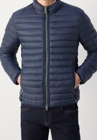 Giacca leggera imbottita di colore blu navy con cuciture orizzontali, colletto alto e doppie tasche anteriori con zip, realizzata in un materiale liscio e resistente all'acqua.