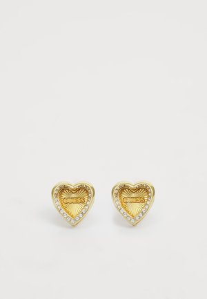 Orecchini a forma di cuore in oro con finitura testurizzata, caratterizzati dal logo "GUESS" e circondati da una fila di pietre di strass trasparenti.