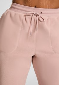 Lichtroze fleece joggingbroek met een gestructureerd oppervlak, elastische tailleband en dessin met trekkoord. Voorzien van twee frontzakken.