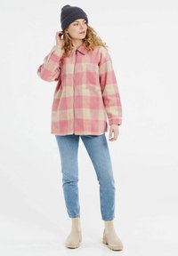 Chaqueta a rayas en rosa y crema con cremallera frontal, cuello y un bolsillo en el pecho, combinada con jeans azul claro y botines beige.