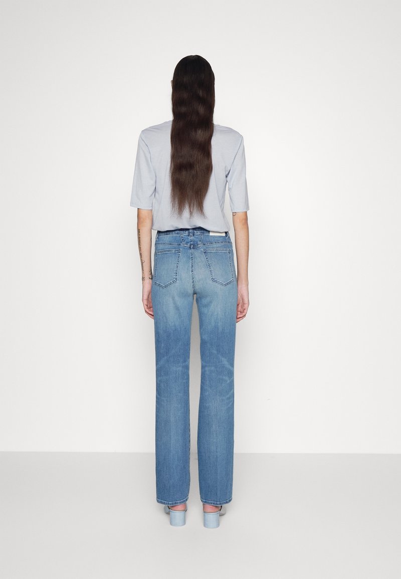 Jean large délavé bleu clair avec une texture fanée, cinq poches et une ceinture standard, associé à un haut gris à manches courtes.