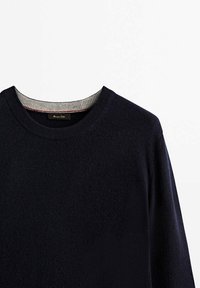 Pull bleu marine avec un col rond, doté d'un col côtelé gris et d'une texture subtile, fabriqué en matière douce. Étiquette du fabricant visible.