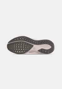 Semelle de chaussure de course en noir et beige avec un motif de grip texturé et le logo Nike sur fond blanc uni.