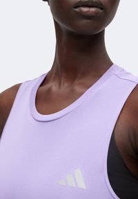 Gros plan d'une personne portant un haut de sport sans manches lavande avec un logo Adidas blanc sur la poitrine.