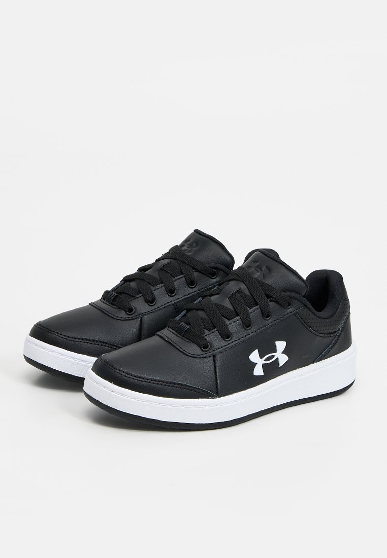 Par de zapatillas negras Under Armour con suelas y logo blancos, cordones negros y diseño de caña baja sobre un fondo claro y sencillo.