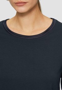 Marineblaues kurzärmliges Oberteil mit einer glatten, weichen Textur und einem runden Rundhalsausschnitt, der mit einem kontrastierenden dunklen Rand versehen ist.