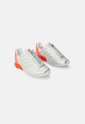 Paar silberne Slip-On-Sneaker mit Frontreißverschluss und leuchtend orangefarbener segmentierter Federsohle auf weißem Hintergrund.