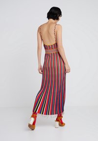 Femme aux cheveux noirs courts portant une robe sans manches à rayures verticales multicolores et des talons orange avec des chaussettes rouges, de dos.