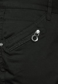 Svarta tygbyxor har en sidoficka med dragkedja och en silverfärgad metalldragare. Texturen verkar slät med subtila sömnadsdetaljer.