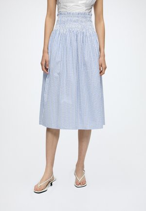 Jupe midi rayée verticale bleu et blanc pour femme avec taille élastique smockée, portée avec des sandales blanches à brides et talons.