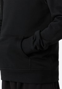 Hanorac negru cu textură moale, prevăzut cu buzunar tip cangur și manșete elastice. Designul include o croială lejeră și cusături minime.