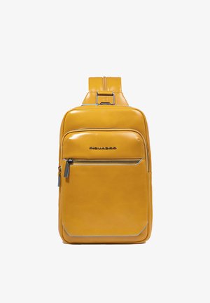 Mochila de cuero amarillo con textura suave, un bolsillo delantero con cremallera y un asa superior. Presenta costuras sutiles y un diseño elegante.