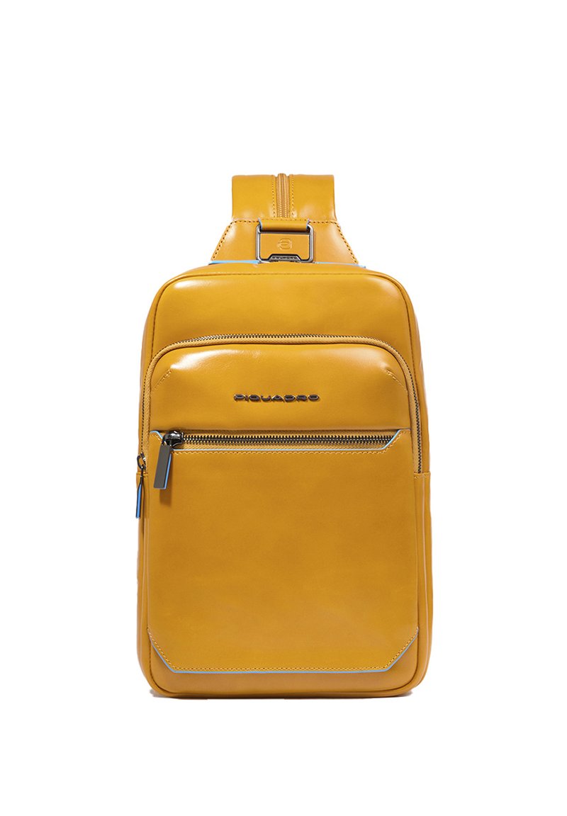 Mochila de cuero amarillo con textura suave, un bolsillo delantero con cremallera y un asa superior. Presenta costuras sutiles y un diseño elegante.