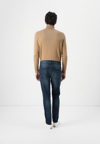 Ruske knit turtleneck, blå slim-fit jeans og hvite sneakers. Fokus på bakvinkel med en jevn, tettsittende silhuett.