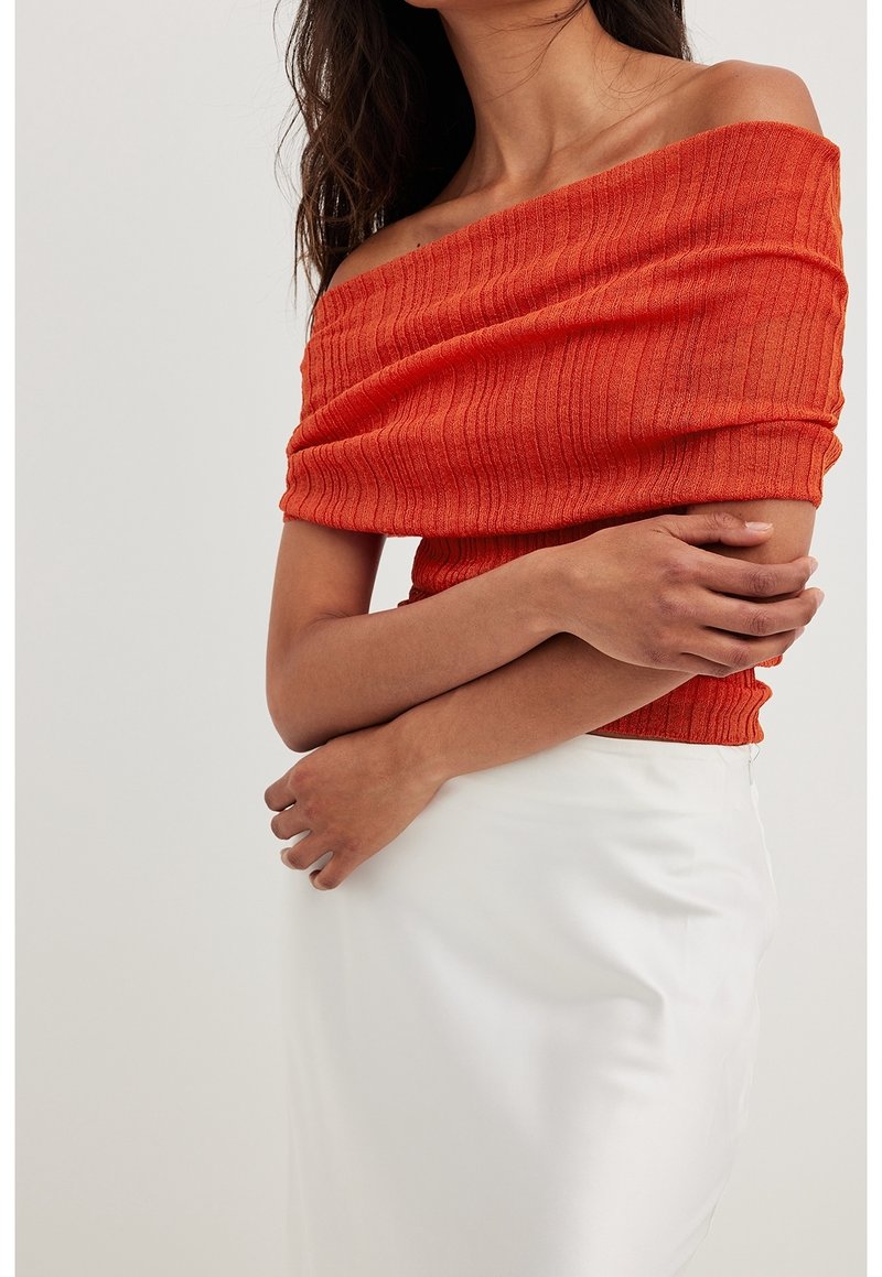Off-the-shoulder, ribbed top in vibrant orange, paired with a smooth, white, knee-length skirt. Features a fitted silhouette and textured fabric.