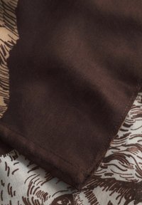 Tissu marron avec une texture lisse, présentant un motif en tons plus clairs. Le bord est fini par un ourlet net cousu.