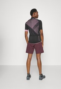 Zwarte sporttop met roze accenten en een geometrisch patroon, gecombineerd met bordeauxrode shorts. Heeft een aansluitend ontwerp, geschikt voor actieve kleding.