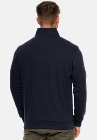Marineblå halv-zip pullover med ribbet krave og manchetter, glat tekstur og lige kant, båret over khaki bukser.